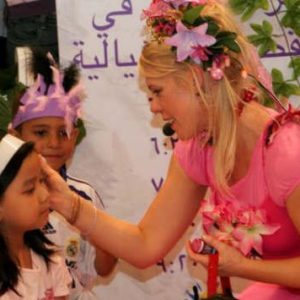 A woman in a pink dress giving a child a kiss.