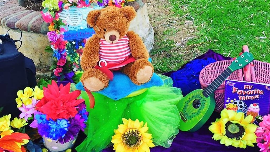 A teddy bear sitting on a pillow next to a guitar and flowers.