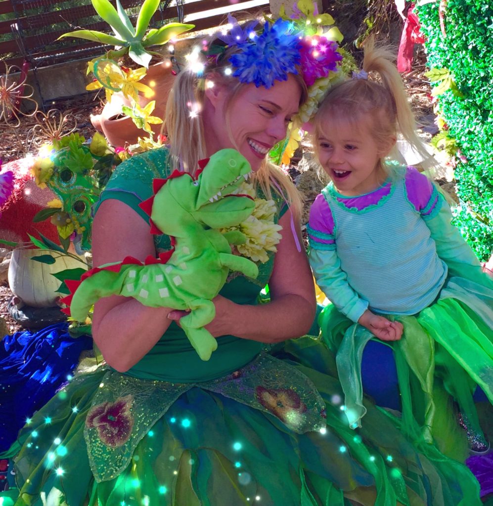 A woman dressed in a green dress with a little girl holding a stuffed animal.