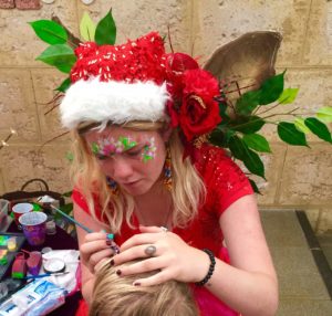 A woman with a santa hat is painting a child's face.