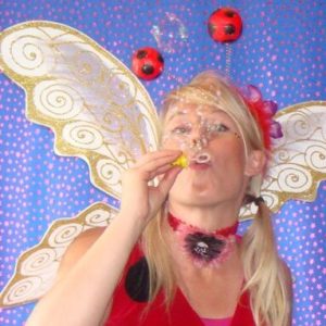 A woman blowing bubbles while dressed as a ladybug.