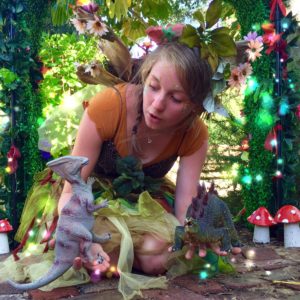 A girl dressed up as a fairy with a toy dinosaur.