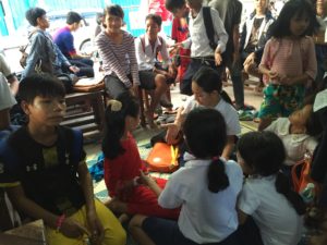 A group of children sitting on the ground in front of a building.