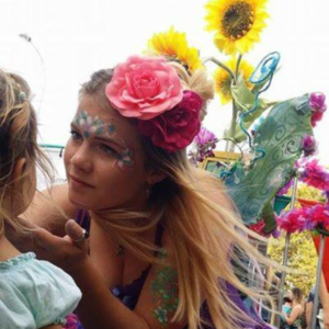 A woman with a flower face painting a little girl.