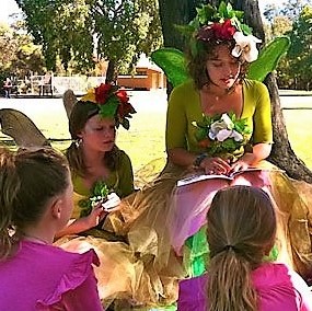 A group of girls dressed up in fairy costumes reading a book.