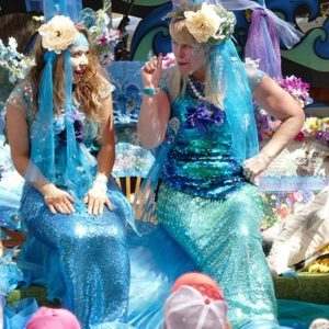 Two women dressed as mermaids sitting on a blanket.