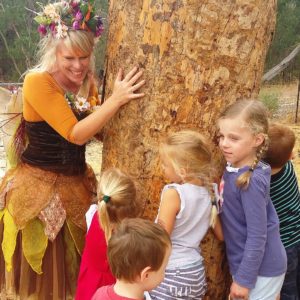 A woman dressed in a fairy costume is standing next to a tree.