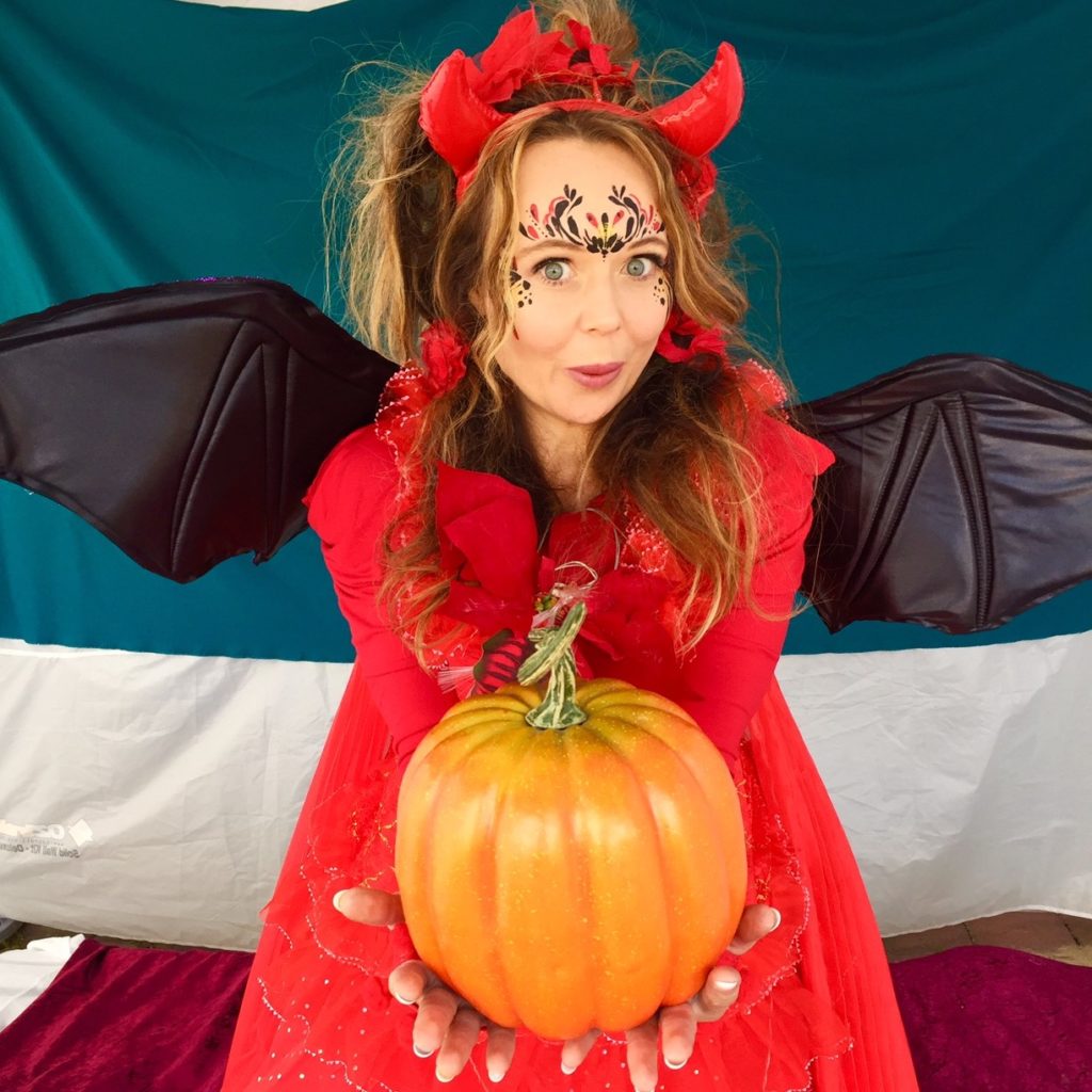 A woman dressed as a devil holding a pumpkin.