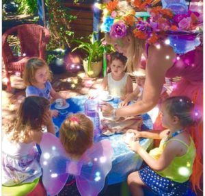 A woman dressed as a fairy sits at a table with children.