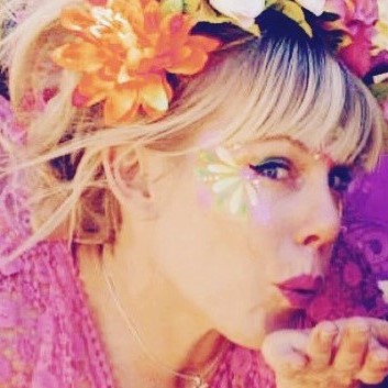 Woman with a floral headband blowing a kiss, featuring a butterfly face sticker, against a purple background.