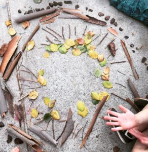 A group of children are gathered around a circle of sticks and leaves.