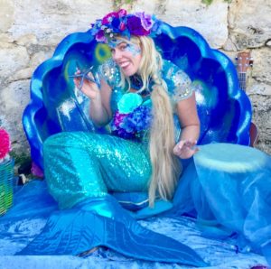 A woman dressed as a mermaid sitting on a blue shell.