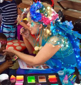 A woman in a blue dress is painting a child's face.