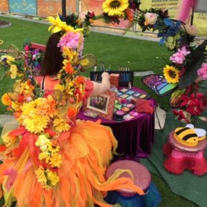 A girl dressed as a fairy sits at a table with flowers.