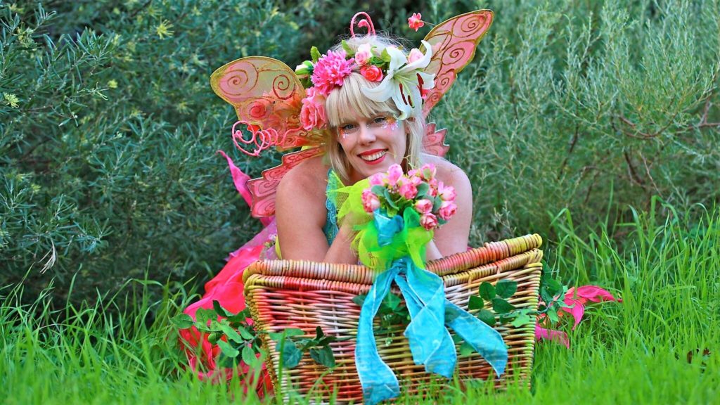 A woman dressed as a fairy holding a basket in the grass.