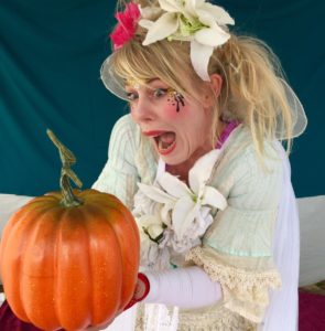 A woman in a costume holding a pumpkin.